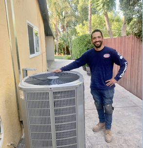 Kilowatt HVAC Technician stands proudly with his hand on a newly installed heat pump.