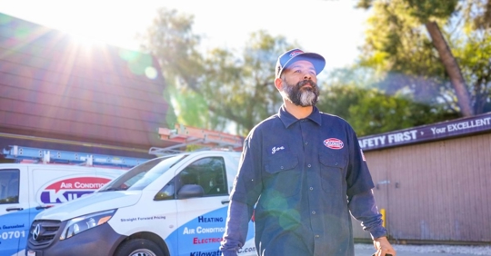 Kilowatt electrician walking outside, with intense summer heat and the service truck in the background